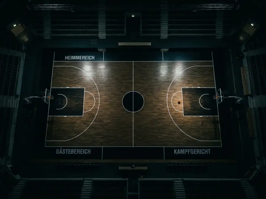 Basketballfeld von oben mit verdunkelter Atmosphäre und einem einzelnen Basketball auf dem Freiwurfkreis